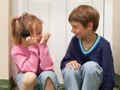 little girl  listening to music with headphones and talking with a boy laughing sitting on doorstep outside