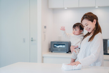 赤ちゃんを抱っこしながら家事をするお母さん © maroke