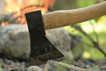 Hatchet lodged in a log of wood, situated opposite a campfire