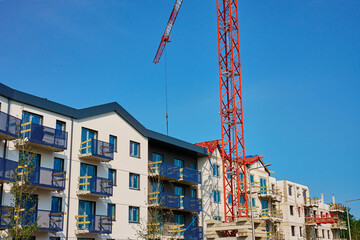 Red construction crane is building modern apartments in residential complex against blue sky....