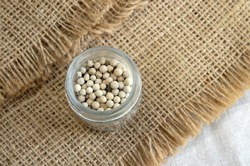 Spices, white peppers, pepper seeds sprinkled on white textured background, close-up