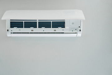 White air conditioner unit is mounted on wall, ready for maintenance. Climate system with opened front cover revealing internal components. Repairing HVAC in apartment