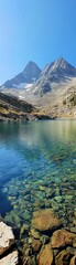 Pristine mountain lake, emerald water, rocky shore, towering peaks, clear skies, wide shot, peaceful and aweinspiring