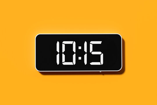 Black digital alarm clock showing 10:15 on yellow background