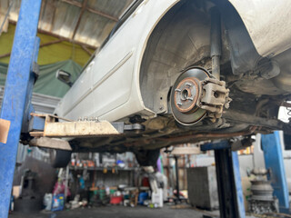 A car being serviced on lift in garage, showcasing undercarriage and brake components.