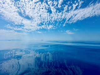 White clouds in the blue sky over a water. Reflection of white clouds and blue sky clouds in the water. Atmospheric natural background.