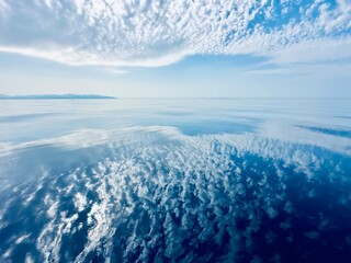 White clouds in the blue sky over a water. Reflection of white clouds and blue sky clouds in the water. Atmospheric natural background.