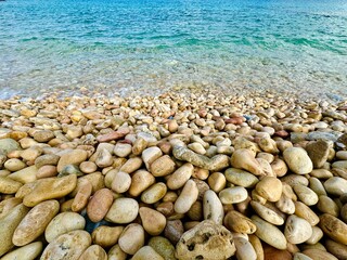 Wet pebbles on the seashore. Bokeh, selective focus. Blue water. Clean clear sea water. Bright sunny day, holidays. Sea travel, ocean vacation. Mediterranean style. Sea resort.