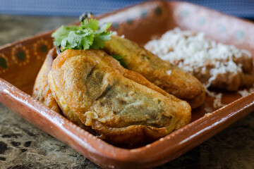 Front view of three stuffed chiles next to beans. Mexican food