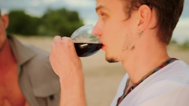 Sweet conversation with a glass of wine on a romantic date of two young gays looking into each other's eyes on the beach close-up. Soft focus.