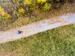 Obraz premium Aerial view of a runner running through autumn park on jogging path with fallen leaves. Morning running training.