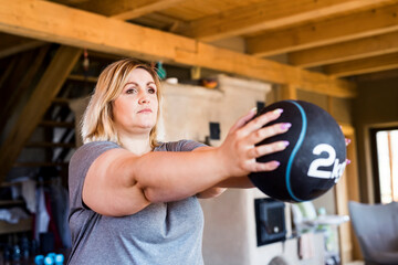 Overweight woman exercising at home, using weighted medicine ball. Workout in living room.