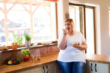 Portrait of beautiful young overweight woman choosing healthy food, eating vegetable salad. Beauty and body positivity concept.