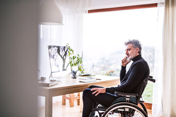 Handsome man in wheelchair working from home office, making phone call. Telecommuting and home office.