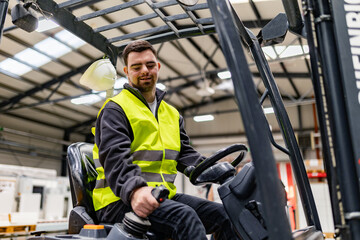 Fototapeta premium Portrait of young man with Down syndrome driving forklift, working in factory, warehouse. Concept of workers with disabilities, support in workplace.