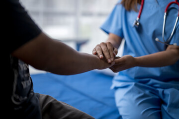 Female doctor comforting patient by holding his hand in hospital room