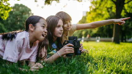 Young girl students learning about nature and wildlife in urban environment, using binoculars and observing animals in public park.
