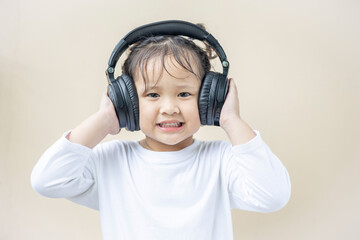 Asian preschool girl wearing wireless headphones listening to music.