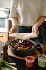 Unrecognizable woman holds hake fillet in her hands over a frying pan with vegetables