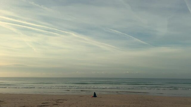 A lone person sits on the beach, gazing at the distant sea horizon. The scene, set in coastal Spain, embodies peace and serenity, capturing a sense of solitude and calm reflection.