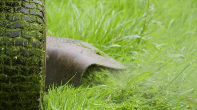 Ride-On LawnMower Moving Foward Through Overgrown Green Grass as Wheels Turn and Blades Cut Grass to Manageable Size 4K