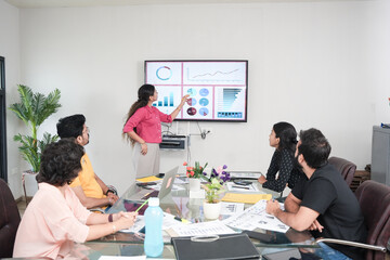 Young indian woman explaining about company growth to other employees on tv screen with Data, Statistics, graph charts. sales, revenue, analysis and Strategy concept.