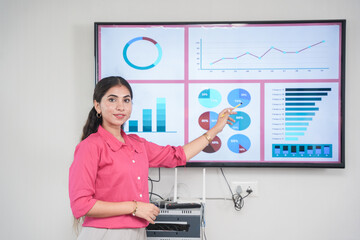 Young indian woman uses tv screen with with Data, Statistics, graph charts, to show company growth to other employees. sales, revenue, analysis and Strategy concept.