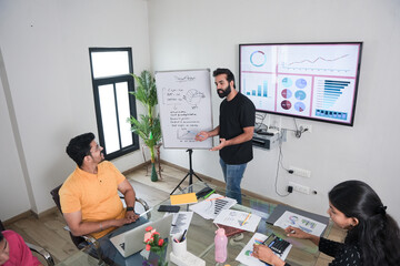 young indian man entrepreneur present business financial data on whiteboard at the workplace to colleagues for a start-up project. sales, analysis and strategy, Entrepreneurship 