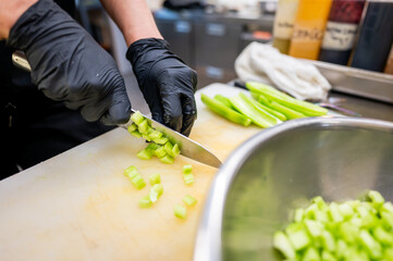 A person wearing black gloves is cutting fresh green celery on a white cutting board with a knife....