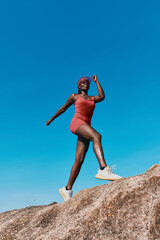 Fit woman exercising on a rocky surface against a clear blue sky