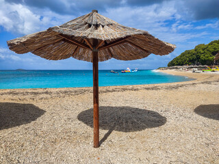 Primosten, Croatia - Reed beach umbrella parasol on Primosten peninsula with turquoise Adriatic sea water, water playground on a sunny summer day with blue sky