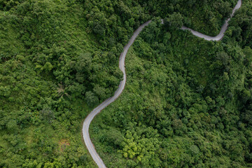 Aerial view on mountain road from drone of road in the middle of the forest in rainy day in spring, green foliage in empty asphalt road through the mountains.