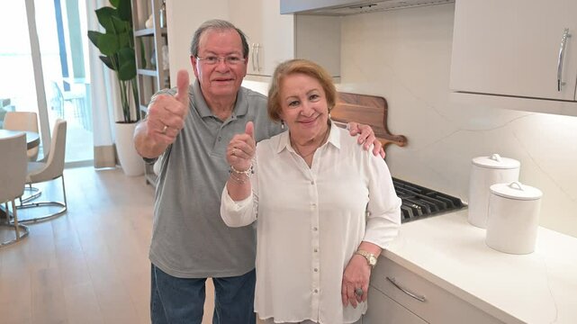 happy customers stand inside their new kitchen by the stove cooktop, and give a thumbs-up sign with their hands approving of the service