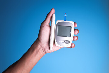 Hand holding glucose meter and injections for insulin on a blue background. Diabetes concept.