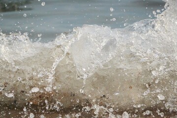 White foam and sea water drop splashes slow motion with sand and blue water