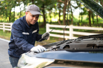 Asian male professional auto mechanic doing onsite service Open the bonnet to check for a broken engine. Inspect the listed damage and maintain emergency assistance services.