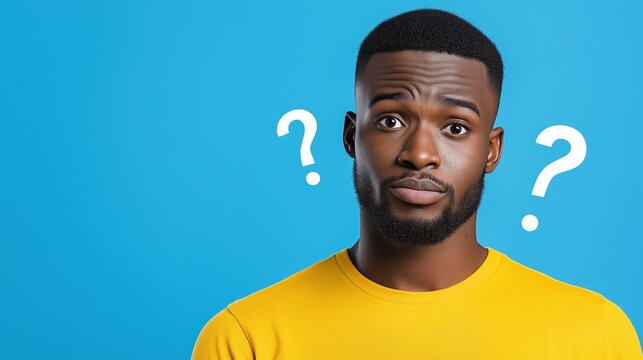 A man with a yellow shirt and a black beard is looking at the camera with two big questions on his face