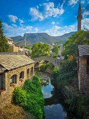 A stunning view of the Stari Most bridge spanning the Neretva River in Mostar, Bosnia and Herzegovina. In the background, a mosque and minaret rise against the historic cityscape. Old city.