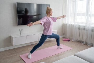 Practicing yoga, a woman is in her cozy living room, surrounded by calm energy and natural light