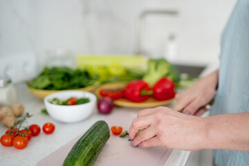 A woman is seen from above, cutting a cucumber in a setting of fresh vegetables