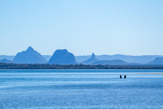 Two fishermen wading in Pumicestone Passage, with the Glass House Mountains in the background.
