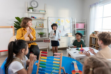 Caucasian young woman teacher playing guitar with students in school. 