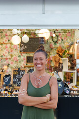Proud Hispanic Woman in Her 50s Posing with Tools in Hand in Front of Her Street Stall Selling Handmade Aluminum Wire Jewelry