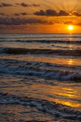 Obraz premium The sun is setting over the ocean, casting a warm glow on the water.