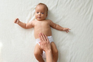 Caring mother making massage to her newborn baby on bed at home unrecognizable woman helping infant kid to relieve gas doing exercises with little kid to prevent child constipation