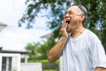 Senior asian man experiencing tooth pain, holding his cheek with pained expression, discomfort and common issues related to dental health, toothache, pain relief, and medical care for seniors at home