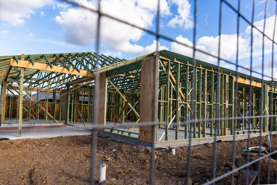 timber framed house build under construction through a security fence