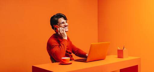 Business consultant in a vibrant orange monochromatic space, handling a client call and using a laptop