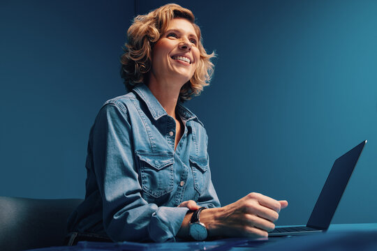 Mature blonde woman with short hair working on laptop in monochromatic office