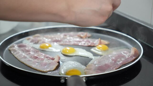 A person is cooking bacon and eggs in a pan